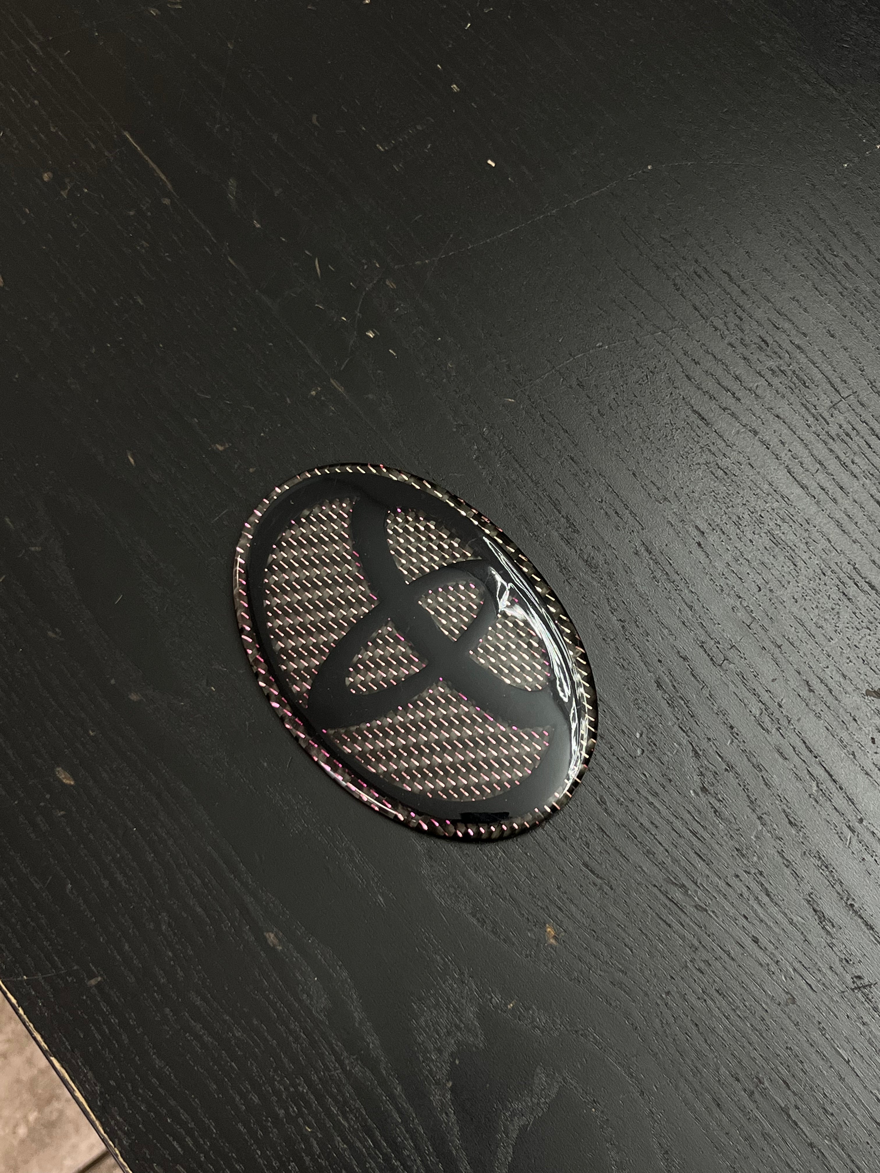 Custom Carbon Fiber Toyota Emblem - Gloss Black Logo with Pink Iridescent Weave.